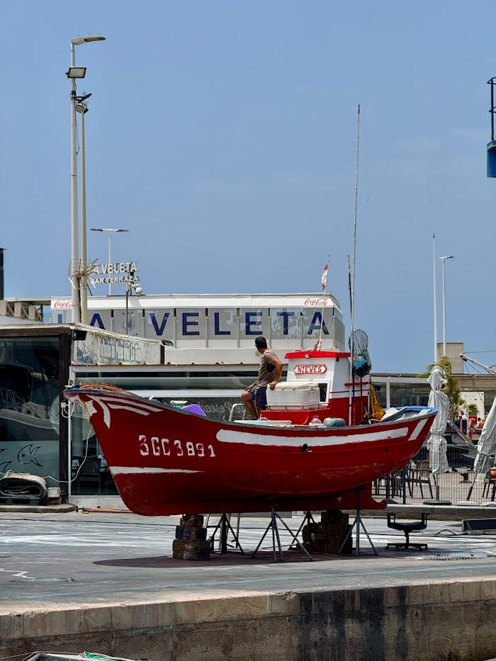 Red fishing boat on an industrial dock in Lanzarote under a clear sky.